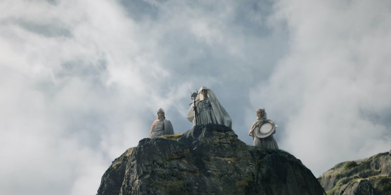 Three white-clad figures stand on top of a rock in The Lord of the Rings: The Rings of Power Episode...