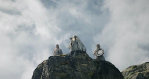 Three white-clad figures stand on top of a rock in The Lord of the Rings: The Rings of Power Episode...