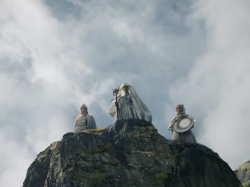 Three white-clad figures stand on top of a rock in The Lord of the Rings: The Rings of Power Episode...