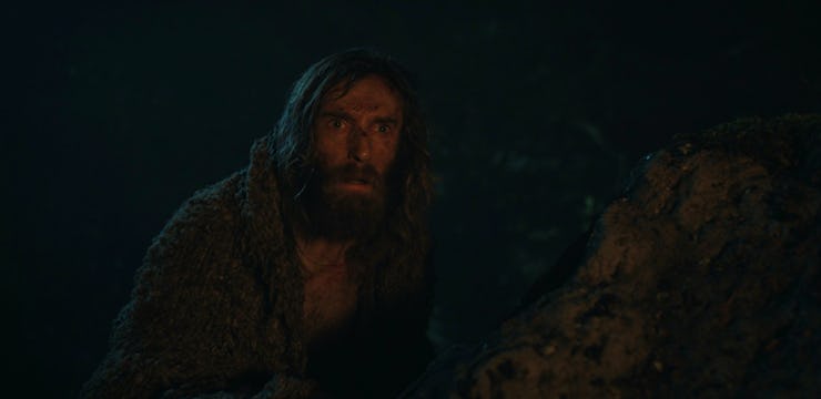 The Stranger (Daniel Weyman) crouches next to a rock in The Lord of the Rings: The Rings of Power Ep...