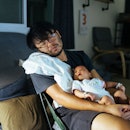 A dad sleeping in a chair with baby in his lap.