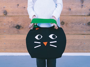 Child holding a black cat trick or treat tote from KiwiCo