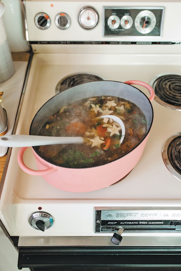 Molly Yeh's Chicken and Stars Soup recipe: the soup cooking on the stovetop in a pink pot