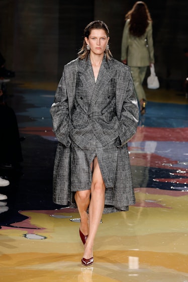 A model walks the Bottega Veneta Spring 2023 runway in plaid gray blazer-skirt suit and long coat.