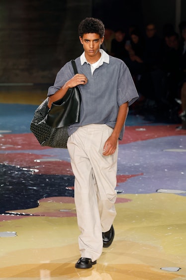 A male model walks the Bottega Veneta Spring 2023 runway in gray t-shirt and white trousers.