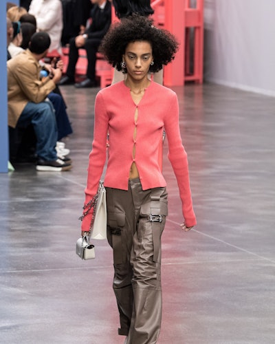 The model wears brown cargos in silky fabrics paired with a peach-colored sweater by Fendi.