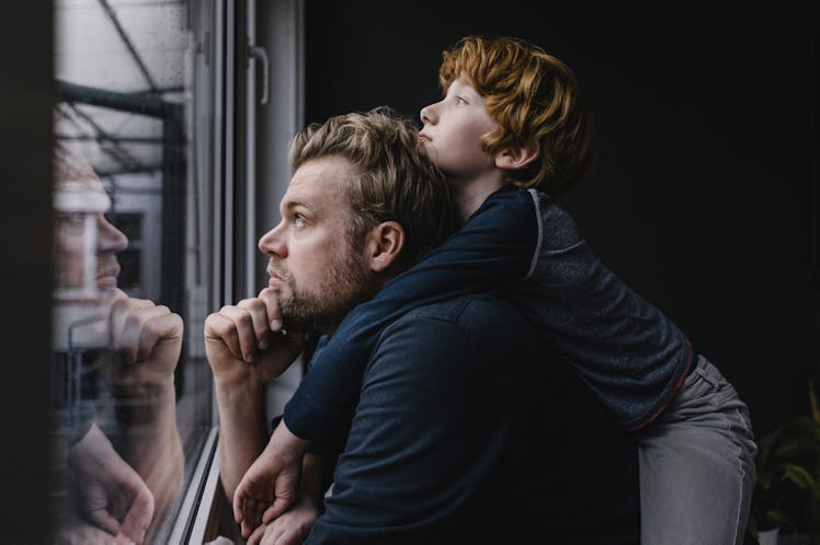 A boy on his dad's back looks out the window at a rainy day.