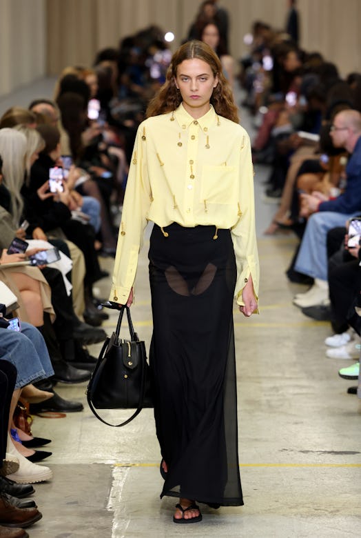A female model walking the runway at the Burberry show during London Fashion Week in a yellow shirt