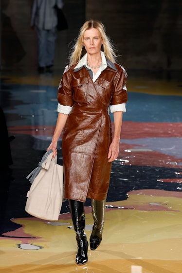A model walks the Bottega Veneta Spring 2023 runway in brown leather coat with white details.