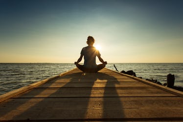 Man sitting cross-legged on a dock, watching the water at sunset.