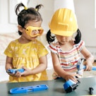 A child in goggles and another in a hard hat play with construction toys.