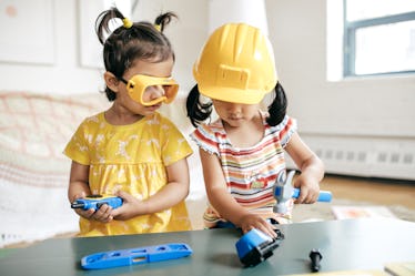 A child in goggles and another in a hard hat play with construction toys.