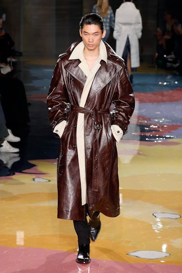 A model walks the Bottega Veneta Spring 2023 runway in brown leather coat with white details.