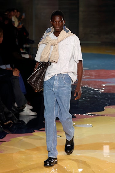 A male model walks the Bottega Veneta Spring 2023 runway in a knitted white t-shirt and jeans.