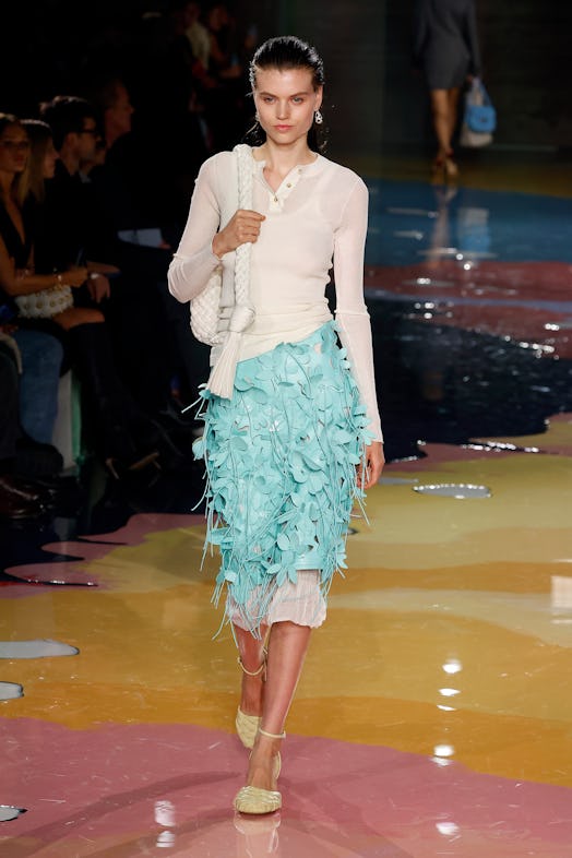 A model walks the Bottega Veneta Spring 2023 runway in turquoise flower skirt and white sweatshirt.