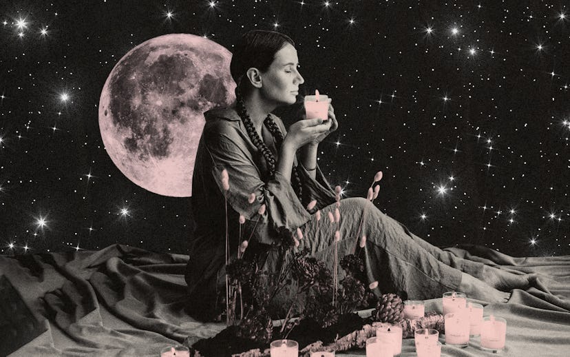 Woman smelling a candle while sitting on a sheet with flowers and candles on it with a background of...