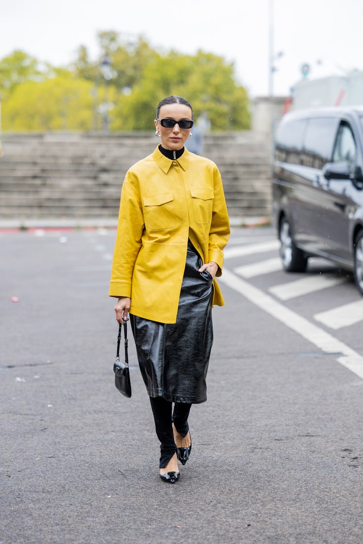 Mary Leest wears yellow button shirt with pockets, black varnished skirt, black Prada bag, black pan...