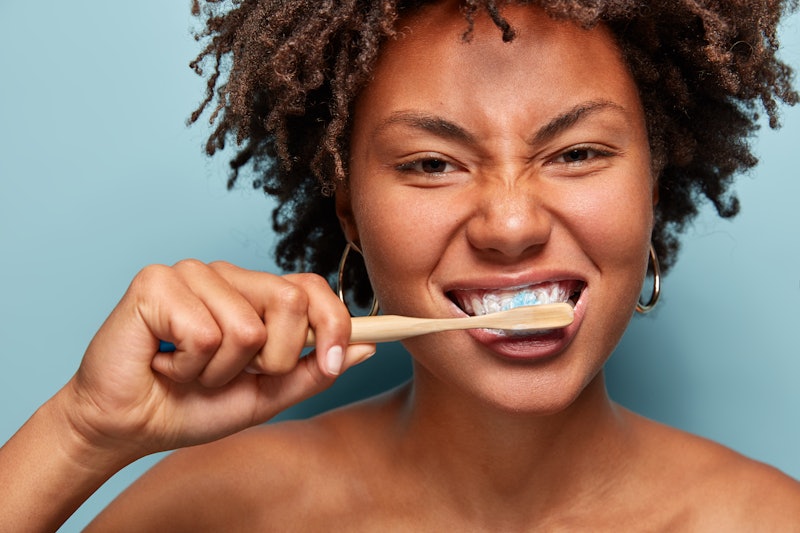 In this photo, a person brushes their teeth with a wooden toothbrush, much like one would for the be...