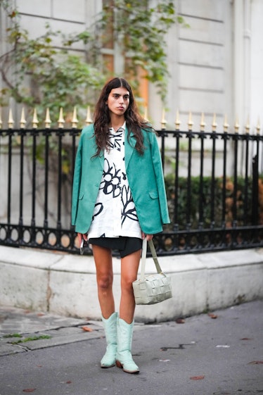 A guest wears a white with black print pattern oversized shirt, a black wrap short skirt, a green co...