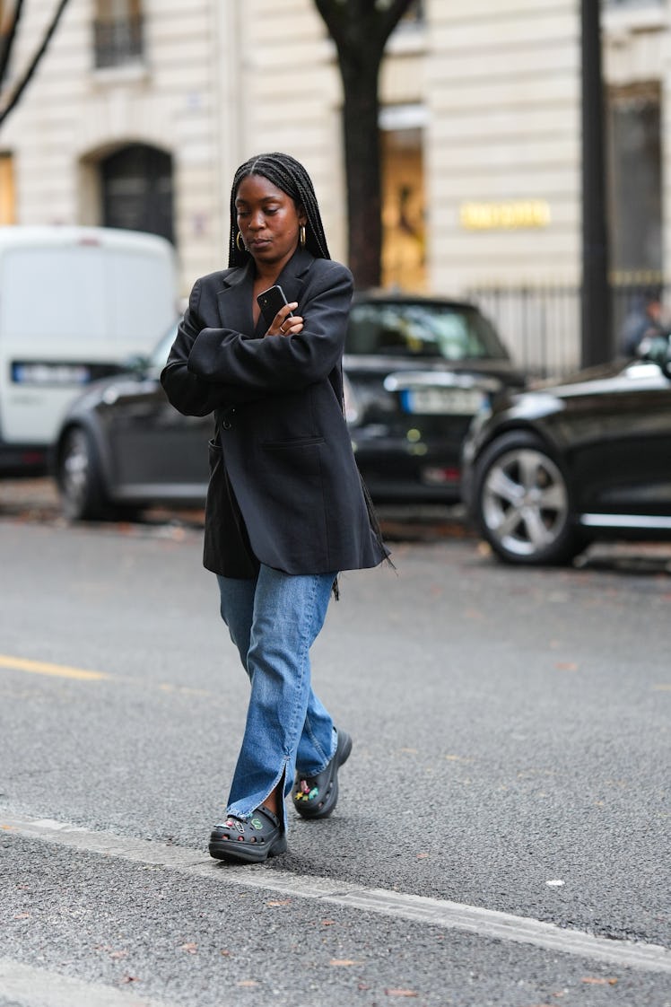 A guest wears gold earrings, a black blazer jacket, blue denim large pants, black plastic with embro...