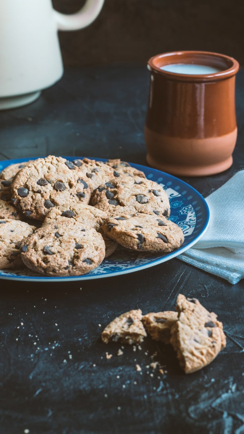 A plate of chocolate chip cookies next to a brown mug full of milk