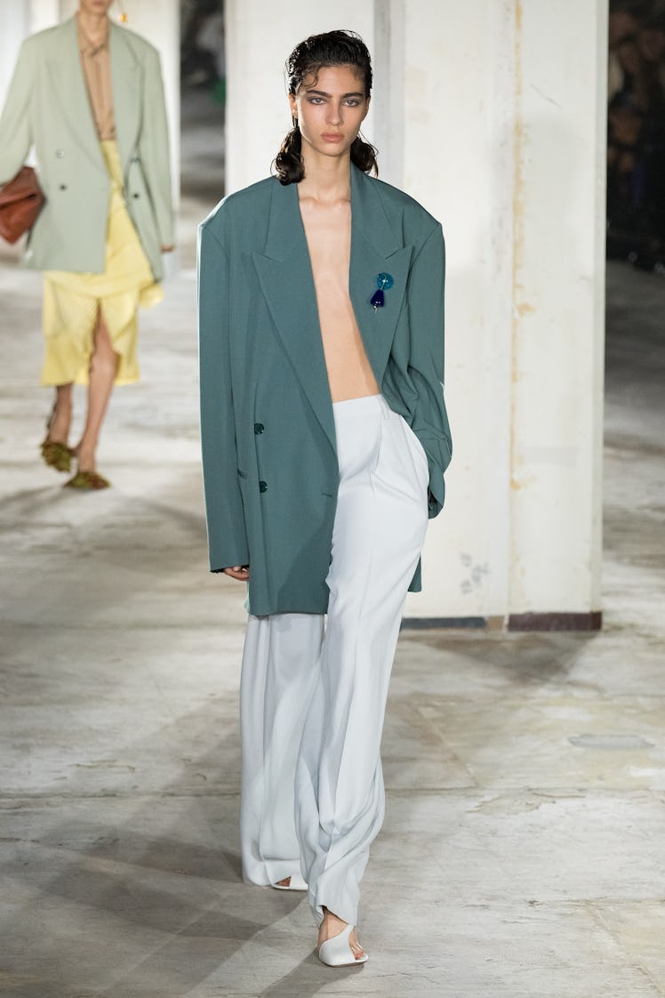 A model wearing Dries Van Noten oversized dark green blazer and white pants at Paris Fashion Week Sp...