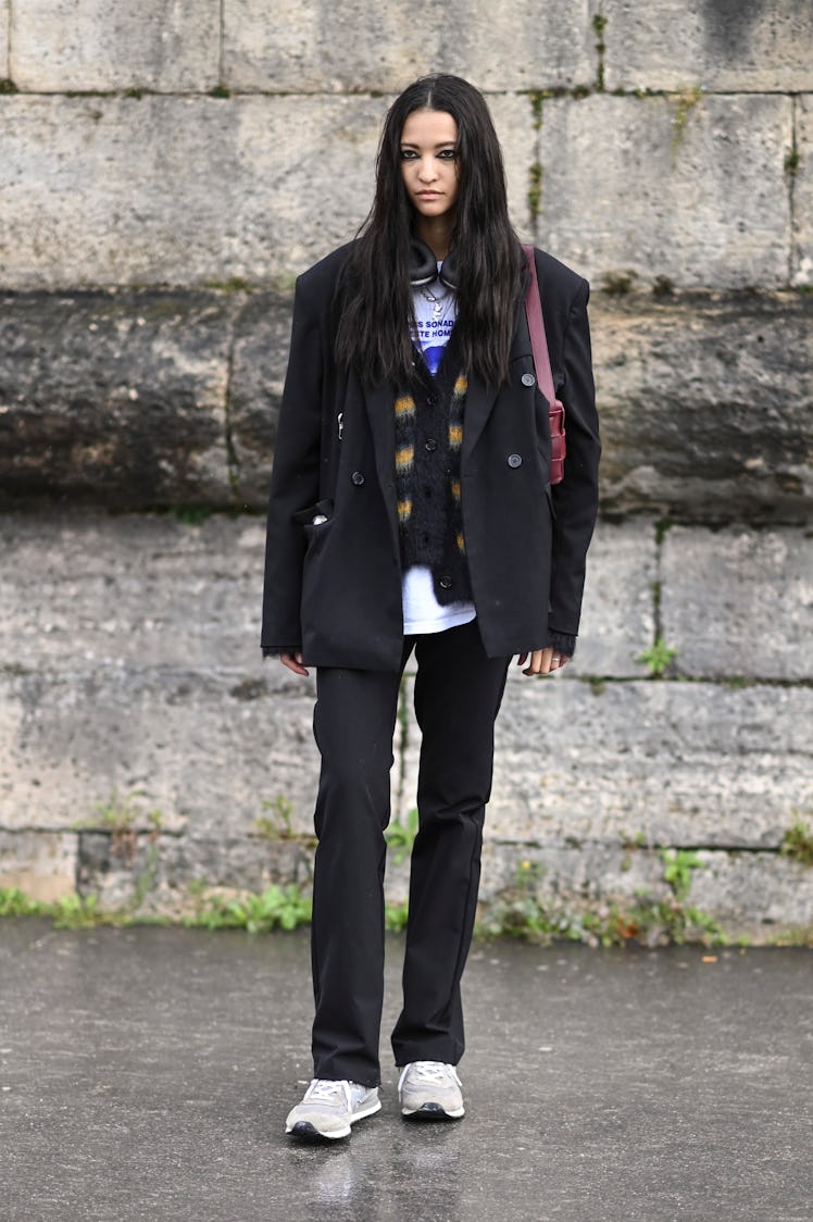 A model is seen wearing a black jacket, black pants and New Balance sneakers with maroon bag outside...