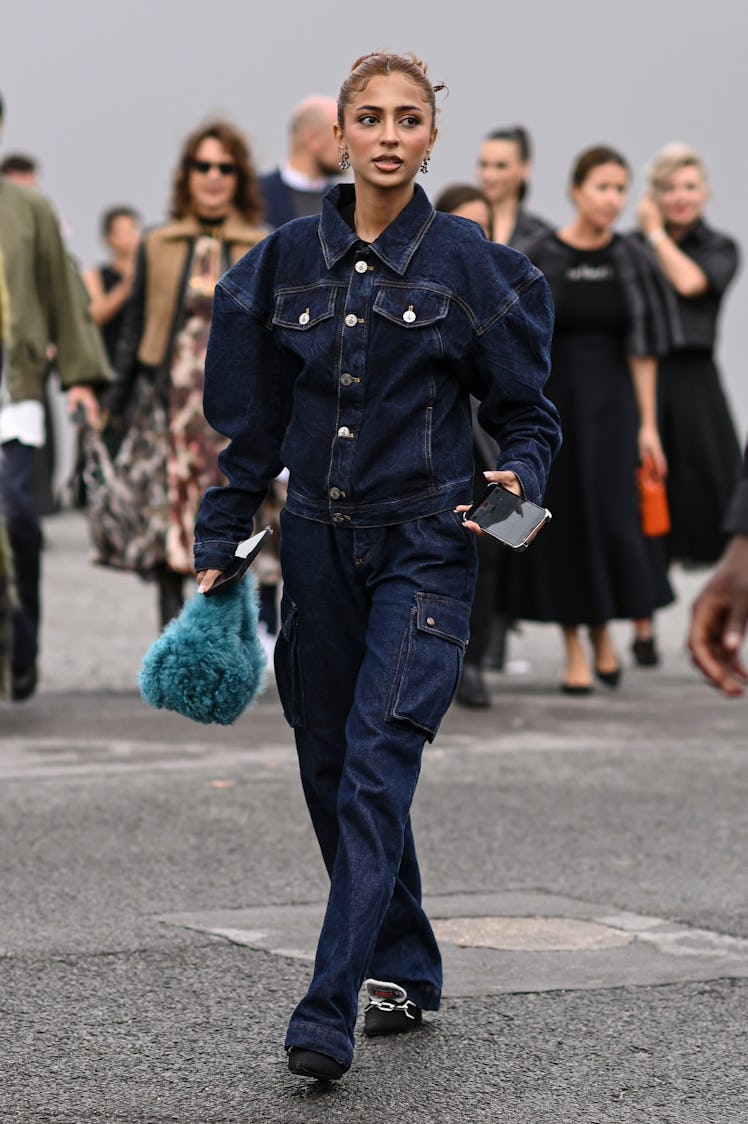A guest is seen wearing a Vivienne Westwood jean jumpsuit and faux fur bag outside the Dior show dur...