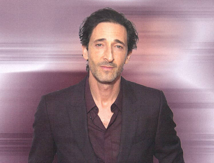 A portrait of Adrien Brody wearing a black suit and brown button down shirt
