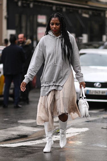 A guest is seen wearing a gray hoodie, cream skirt, white boots and white bag outside the Koche show...