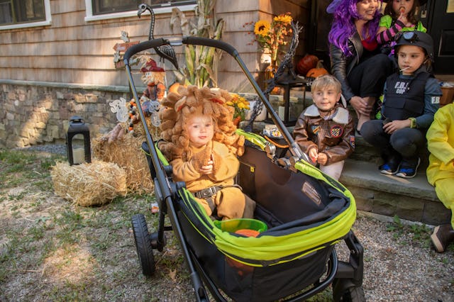 Little baby in all-terrain stroller wagon going trick-or-treating with other kids