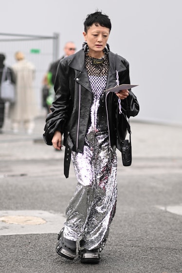 A guest is seen wearing a black leather jacket, silver jumpsuit and black Balenciaga boots outside t...