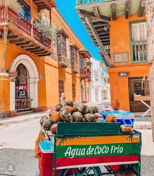 An agua de coco frio stand at a street with orange buildings in Cartagena