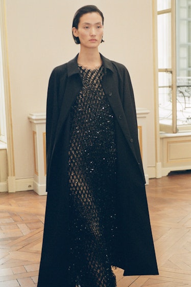 A model wearing The Row transparent, black glitter maxi dress and maxi black coat at the Paris Fashi...