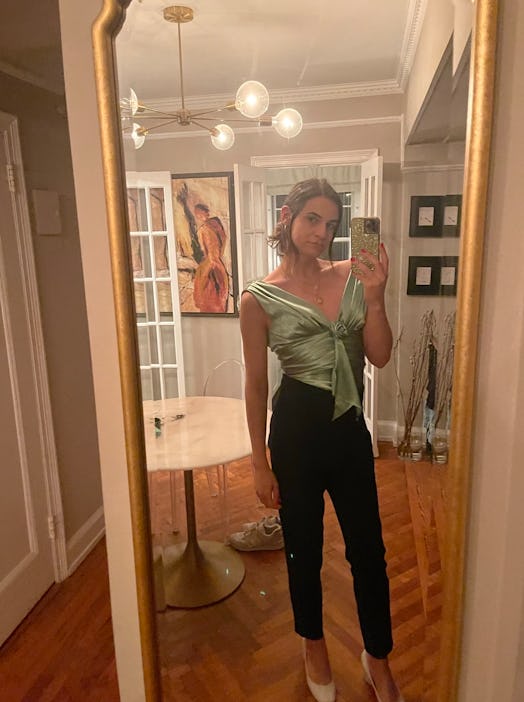 Michaela Malvasio taking a mirror selfie in a sage satin corset top, black trousers and off-white he...