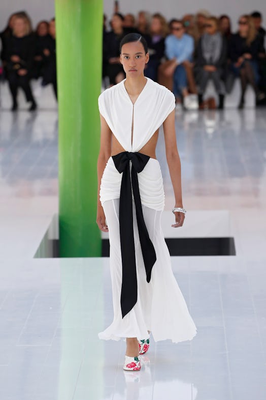 A model walking the runway in a white dress with a big black bowtie on the waist at Loewe Spring 202...