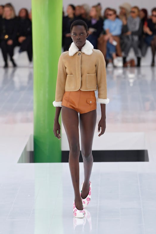 A model walking the runway in a brown jacket and brown leather shorts at Loewe Spring 2023 Paris Fas...