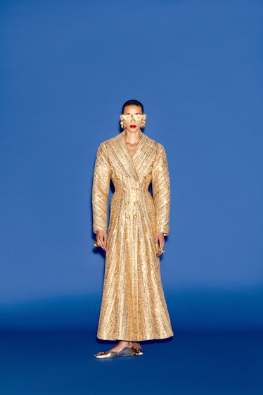 A model in Paris Fashion Week 2023 featured Schiaparelli’s gold maxi coat dress styled with gold sun...
