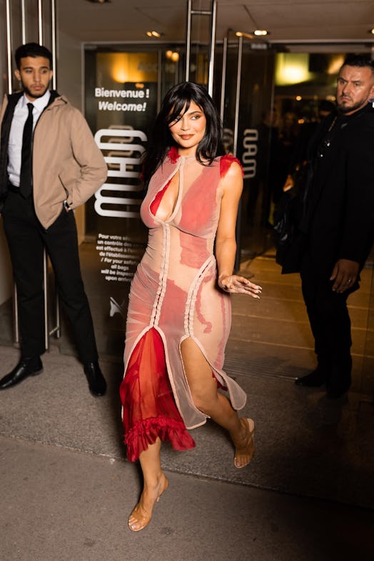 Kylie Jenner wearing a sheer tan and red dress and waving