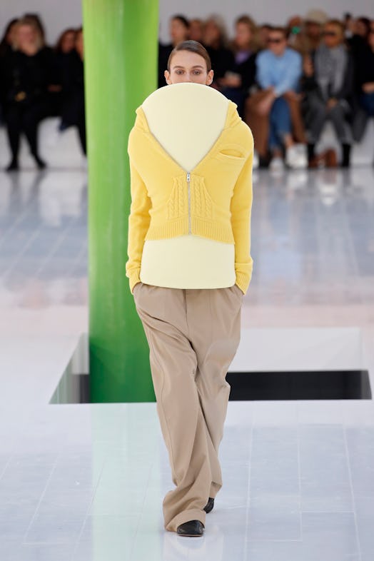 A model in a yellow sweater with a cardboard-like facade obscuring the face at Loewe Spring 2023 Par...
