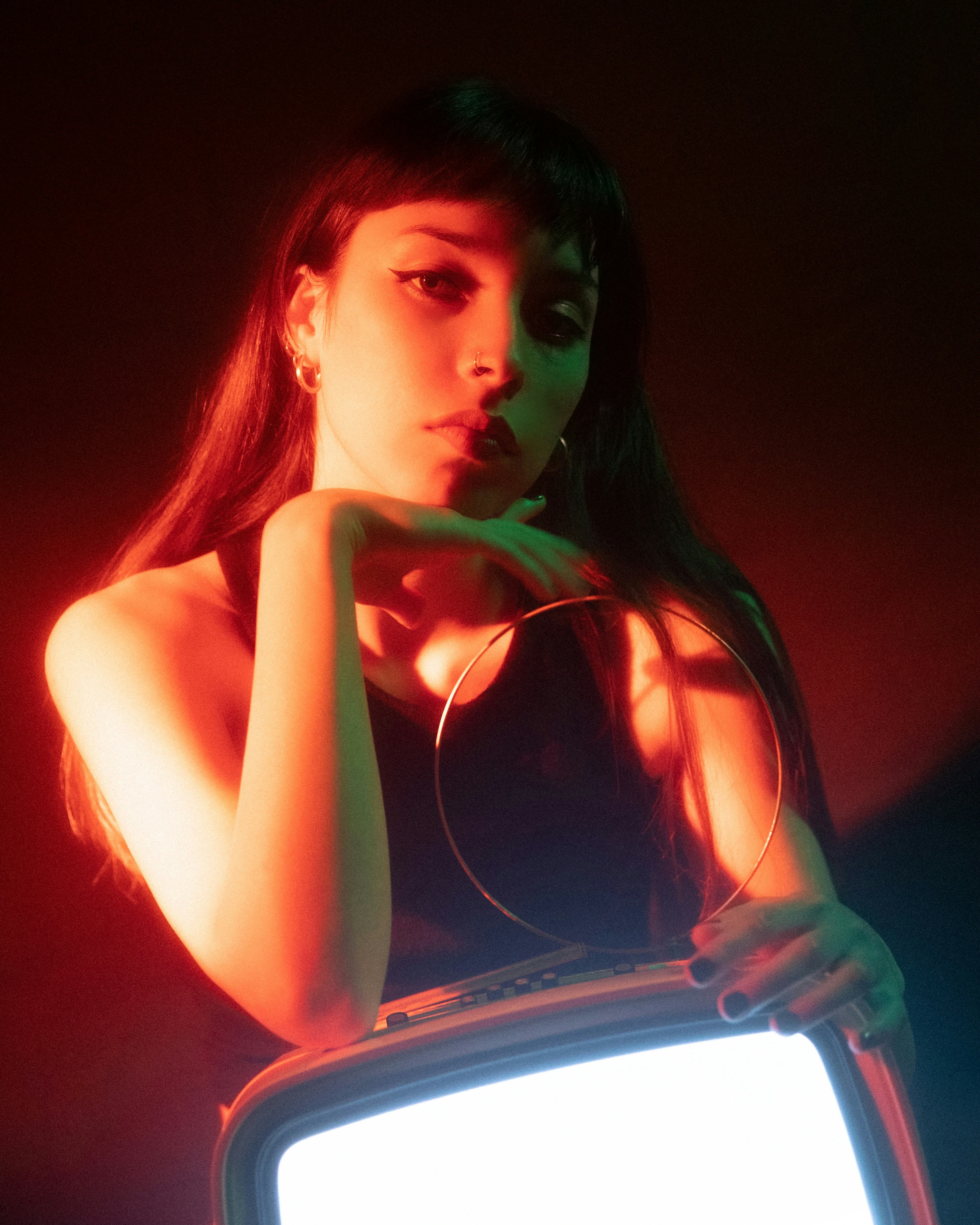 Young woman illuminated by a neon light with a TV monitor as Pluto retrograde 2022 ends.