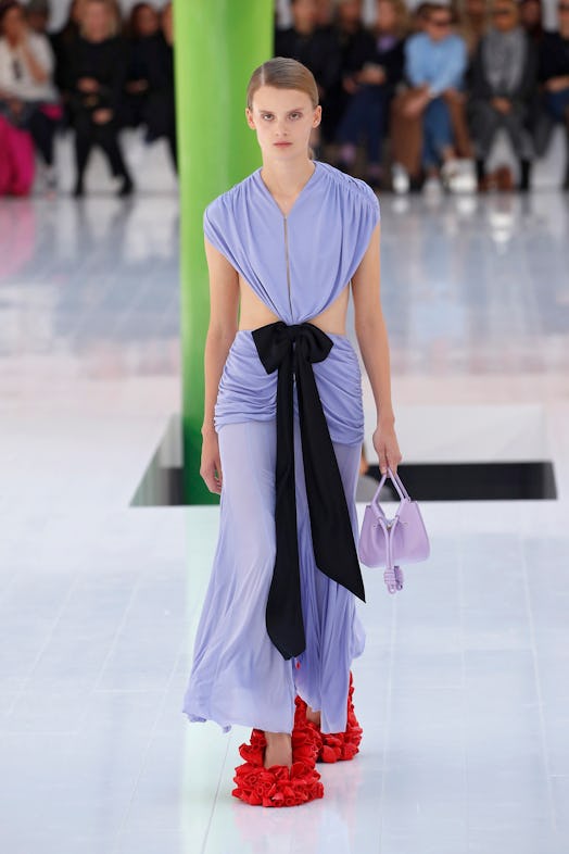 A model walking the runway in a purple dress with a big black bowtie on the waist at Loewe Spring 20...