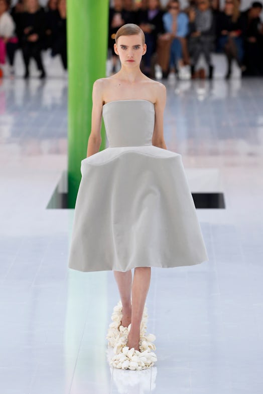 A model walking the runway in a grey dress and white flower shoes at Loewe Spring 2023 Paris Fashion...