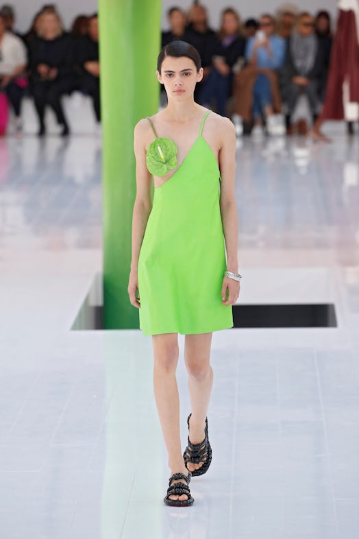 A model walking the runway in a green dress with a green flower covering her breast at Loewe Spring ...