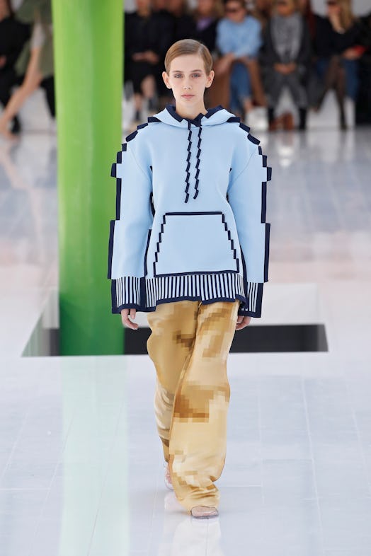 A model walking the runway in a pixelated blue hoodie and pixelated brown pants at Loewe Spring 2023...