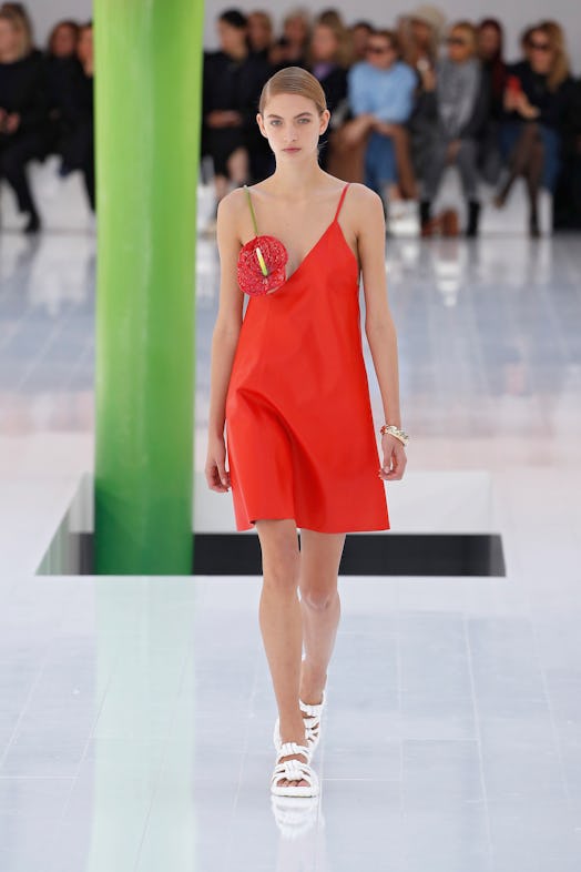 A model walking the runway in a red dress with a red flower covering her breast at Loewe Spring 2023...