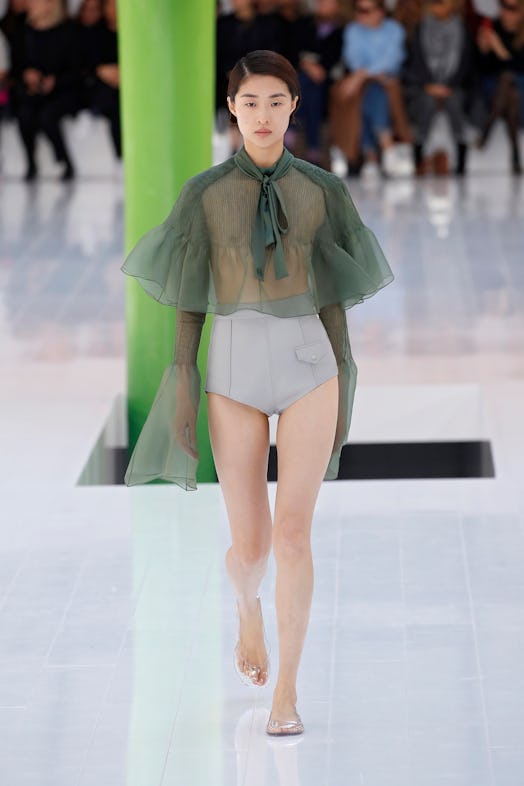 A model walking the runway in a green see-through top and grey leather shorts at Loewe Spring 2023 P...