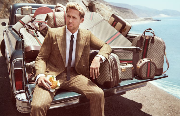 Ryan Gosling surrounded by Gucci monogram luggage and holding a partially eaten hamburger