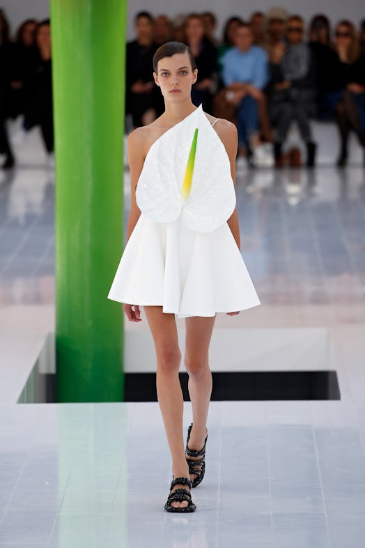 A model walking the runway in a white dress with a giant white flower over her torso at Loewe Spring...
