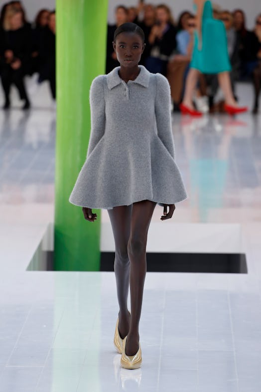 A model walking the runway in a grey woolen dress and golden shoes at Loewe Spring 2023 Paris Fashio...